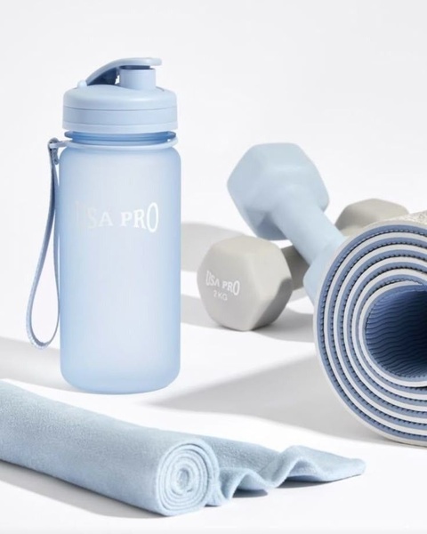 A high-end, studio-lit shot of a blue water bottle, dumbbells, and a rolled yoga mat in a cohesive, minimalist color palette.